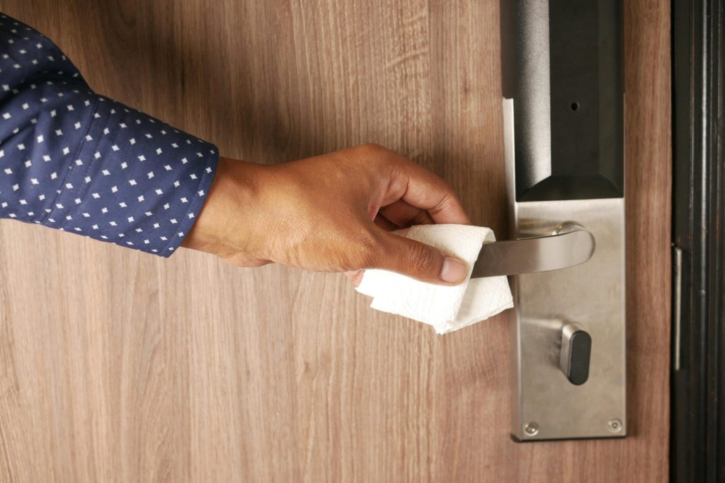 A person cleans a metal door handle with tissue, emphasizing hygiene and safety.